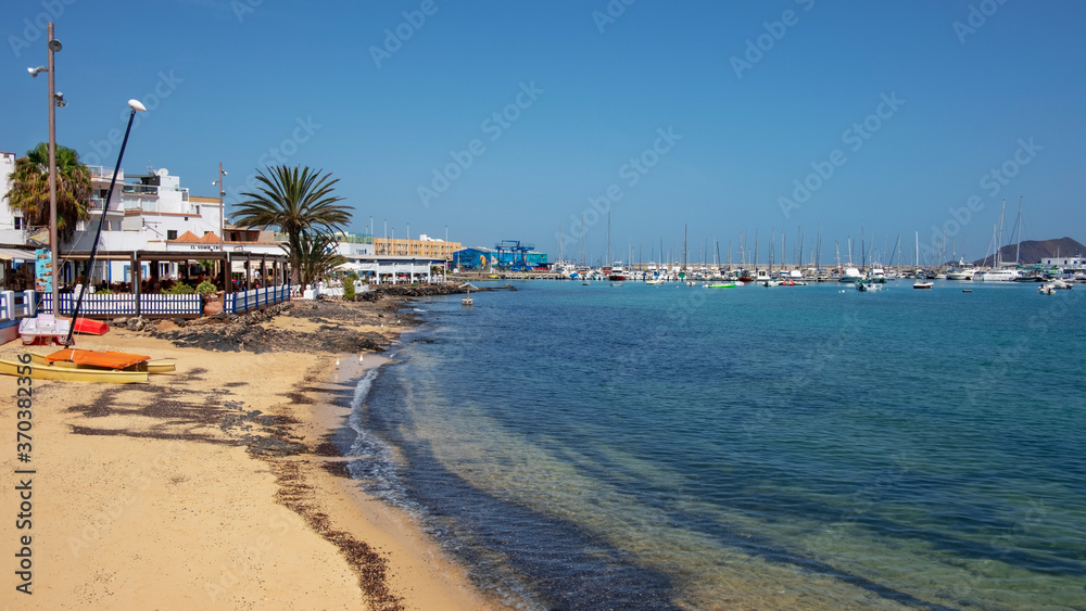 Shallow beach near the promenade, lined up with restaurants and entertainment venues with ample views towards the yachts and vessels, Corralejo, Fuerteventura, Canary Islands, Spain Shallow beach near the promenade, lined up with restaurants and entertainment venues with ample views towards the yachts and vessels, Corralejo, Fuerteventura, Canary Islands, Spain