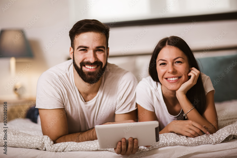 Smiling relaxed young couple using digital tablet in bed at home Smiling relaxed young couple using digital tablet in bed at home