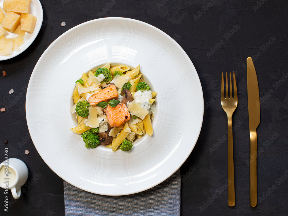 Pasta penne with salmon, broccoli, and pesto sauce on the black background. Flat lay. Pasta penne with salmon, broccoli, and pesto sauce on the black background. Flat lay.