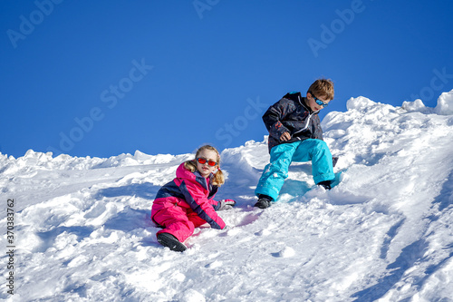 Two joyful kids playing on the snowing mountain on a winter day. Brother and sister