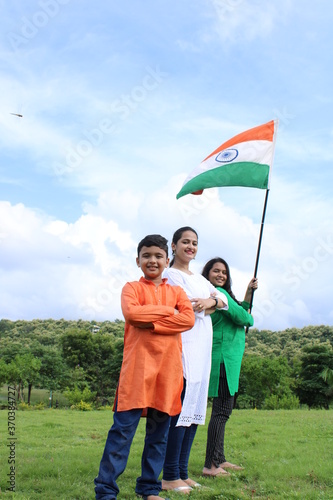 Indian students or children holding or waving Tricolour with greenery in the background, celebrating Independence or Republic day