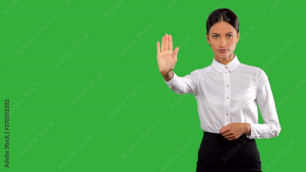 Attractive, young businesswoman making a stop gesture, isolated on green background.