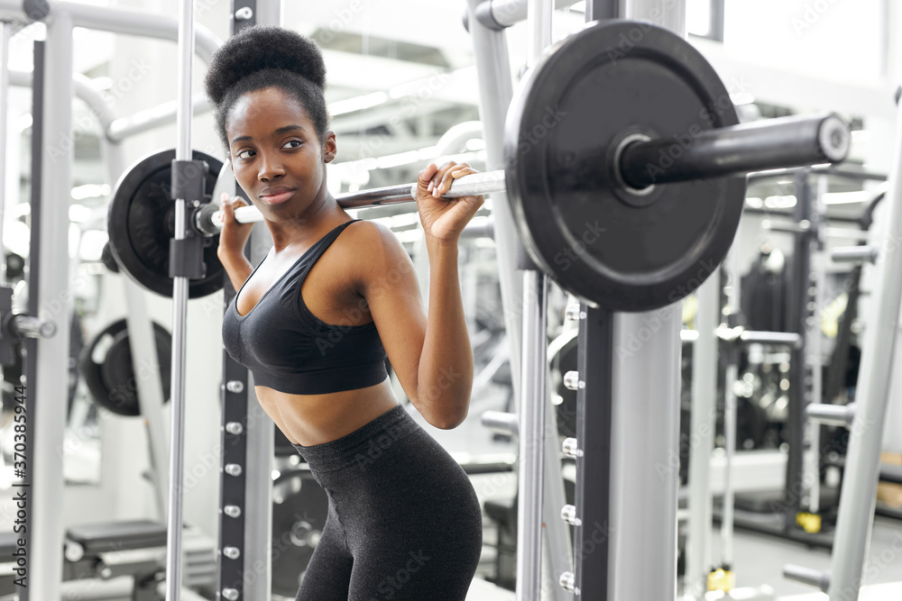 muscular african strong woman lifting heavy barbell pumping biceps in bodybuilding gym muscular african strong woman lifting heavy barbell pumping biceps in bodybuilding gym