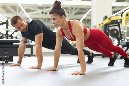 beautiful strong young couple doing push ups together in gym. side view