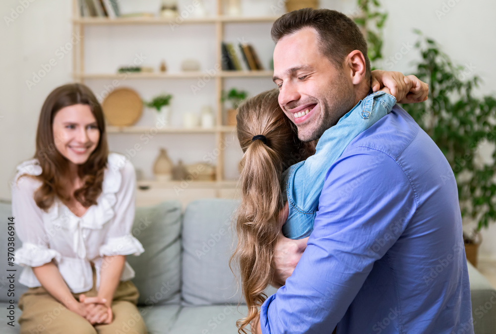 Happy Woman Looking At Husband Hugging Their Daughter At Home Happy Woman Looking At Husband Hugging Their Daughter At Home