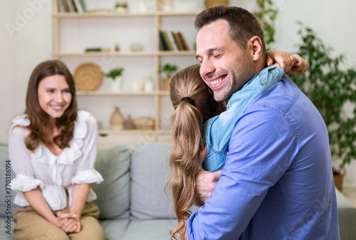 Happy Woman Looking At Husband Hugging Their Daughter At Home