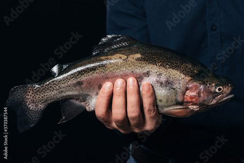 big fish in man's hand on black background. Rainbow trout