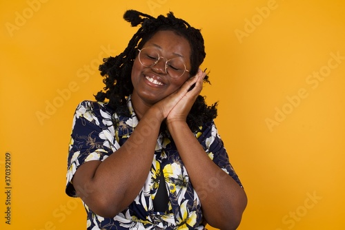 Relax and sleep time. Tired beautiful dark haired girl with closed eyes leaning on palms as pillow pretending sleeping being exhausted seeing dreams standing against gray background. Sleeping gesture.