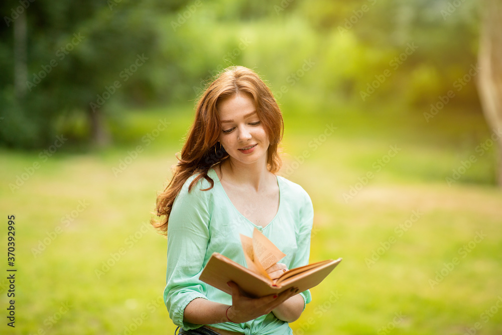 Beautiful Dreamy Redhead Girl Reading Book In Park, Enjoying Time Outdoors Beautiful Dreamy Redhead Girl Reading Book In Park, Enjoying Time Outdoors