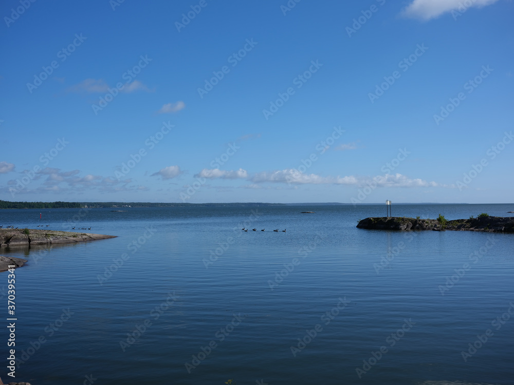View of a lake in Sweden. There are som rocks and some ducks swimming in the water. The water is calm.