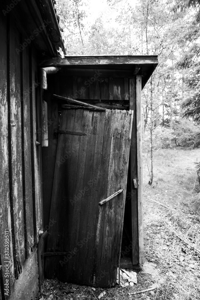 Obraz premium Monochrome photograph of an abandoned house exterior in the woods. This photo shows the door to the outhouse