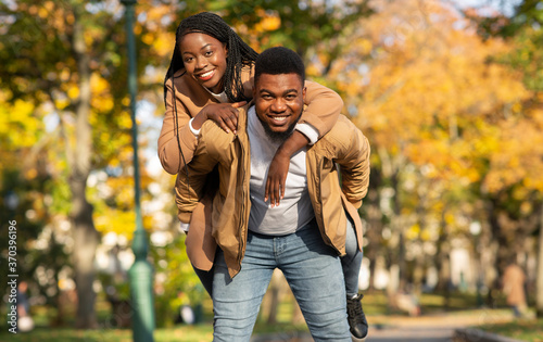 Happy black man carrying his girlfriend on back in autumn park