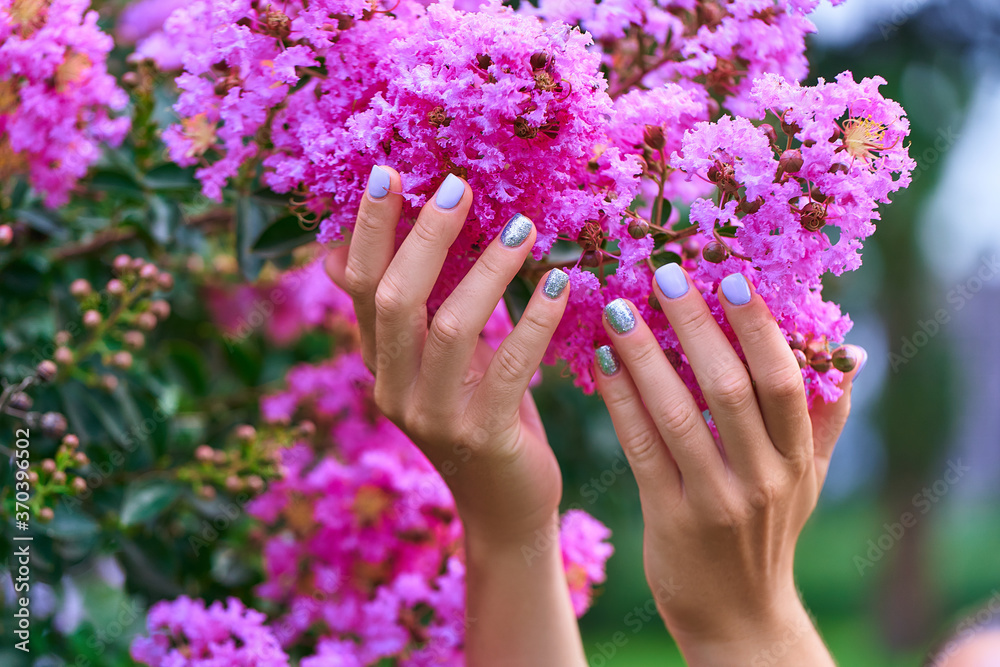 Female manicure with color nail polish and silver glitter against the background of flowers in a park outdoors Female manicure with color nail polish and silver glitter against the background of flowers in a park outdoors