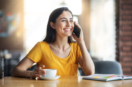 Positive young woman talking on mobile phone at cafe