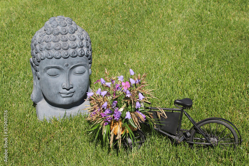 Small Bicycle with colorful flowers in its basket beside bust of Buddha sculpture