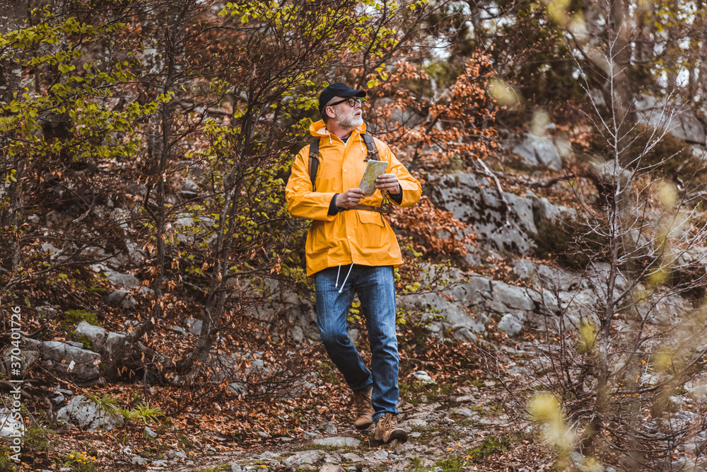 Middle age man traveler in raincoat and backpack enjoying view of mountains.