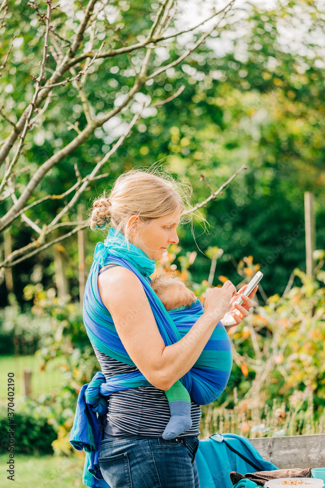 Mother carrying newborn in baby sling while on phone Mother carrying newborn in baby sling while on phone