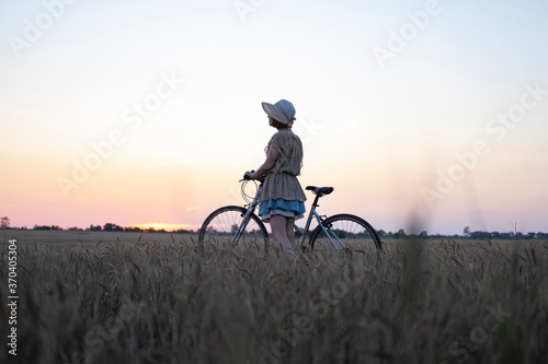 Young woman with hat ride on the bicycle in summer wheat fields