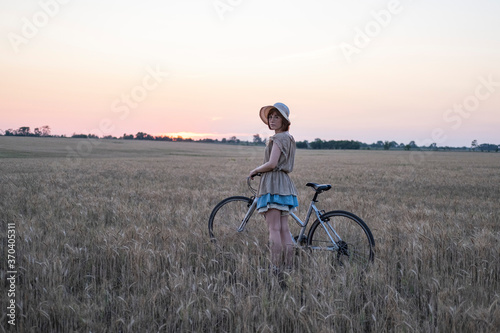 Young woman with hat ride on the bicycle in summer wheat fields