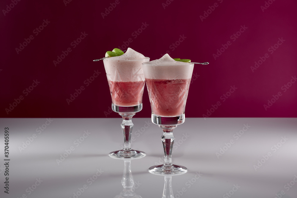 zwei pinke Cocktail Getränke mit grünen Apfel Spießen in alten Kristall Gläsern auf weißer reflektierender Oberfläche mit pinkem Hintergrund