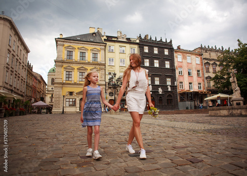 Mother and daughter walk together cheerfully in historic square of old tourist town