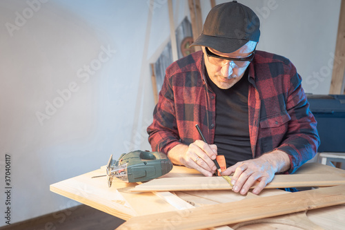 A man works in a carpenter's shop. The master measures the wooden blanks. Joiner working on the order. Electric jigsaw on the table. Carpenter at the joiner's bench.