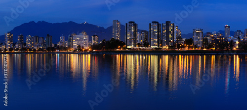 Panorama of West End Vancouver skyline at twilight reflected in English Bay with Grouse Mountain