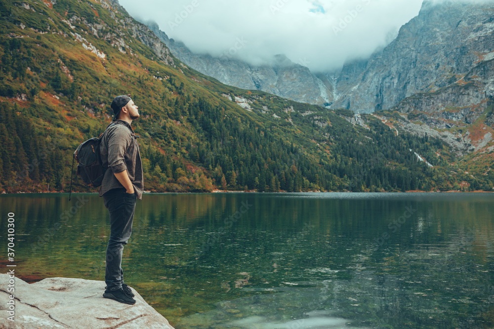 Fototapeta premium man sitting on the rock in front of lake in mountains enjoying the view