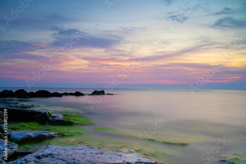 Cloudy summer sunset reflecting in ocean with endless horizon and deep blue ocean, silhouette of boulders laying in the foreground in shallow water at island of Gotland, Sweden