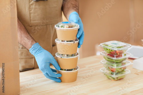 Close up of unrecognizable worker wearing protective gloves safely packaging orders at wooden table in food delivery service, copy space photo