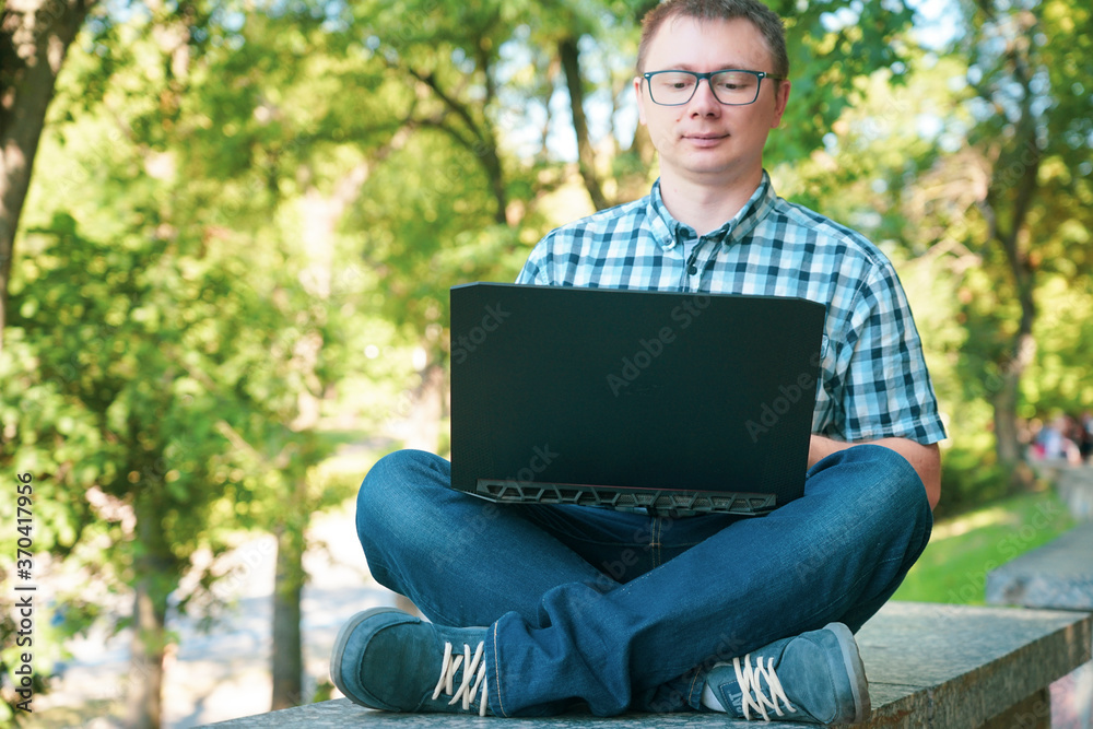 The guy sits in the park and works at a laptop. The guy sits in the park and works at a laptop.