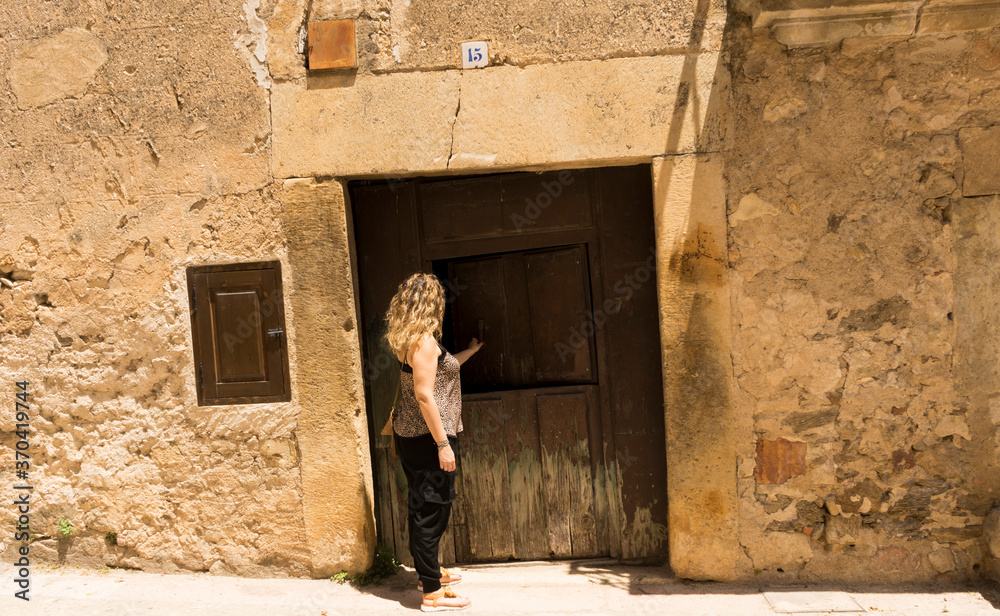 Blonde girl knocking on a village door with facades and cobbled floor3