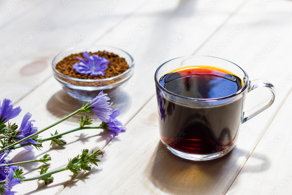 Fototapeta premium Hot natural chicory caffeine free drink in a transparent cup on a wooden table outdoors. Healthy alternative replacement for coffee, caffeine. Blue chicory flower. Beautiful summer morning at nature