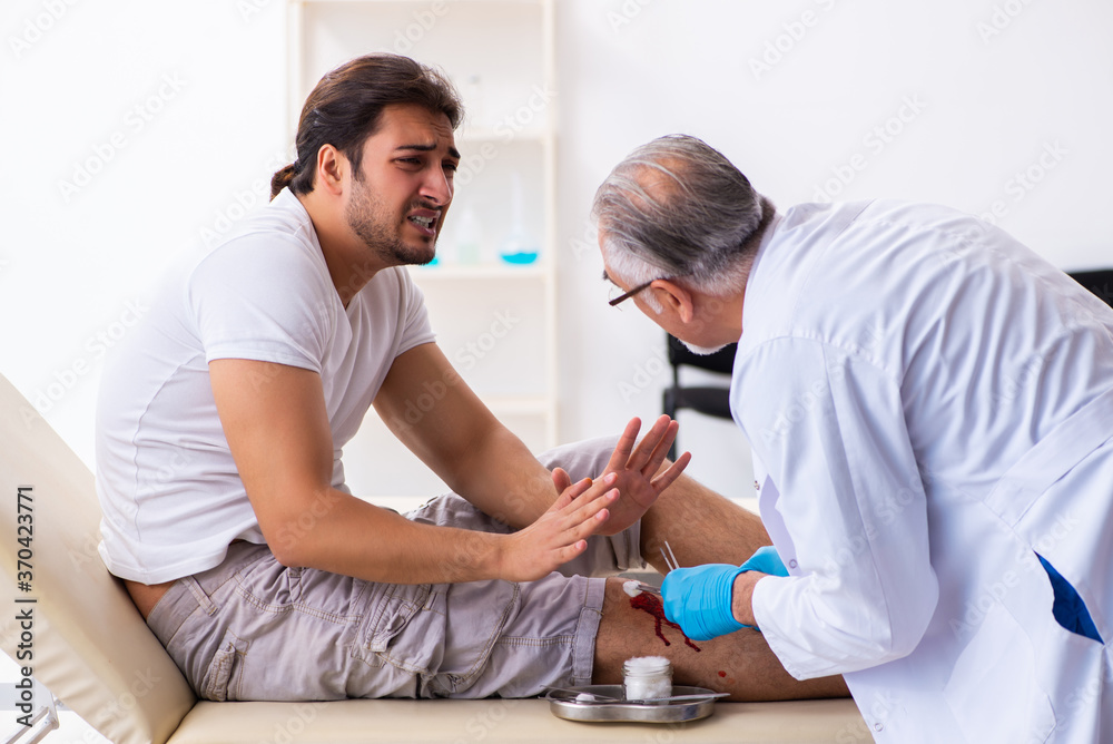Fototapeta premium Leg injured man visiting old doctor in first aid concept