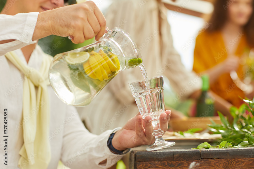 Close up of unrecognizable man pouring lemonade into glass cup while enjoying outdoor party in Summer, copy space