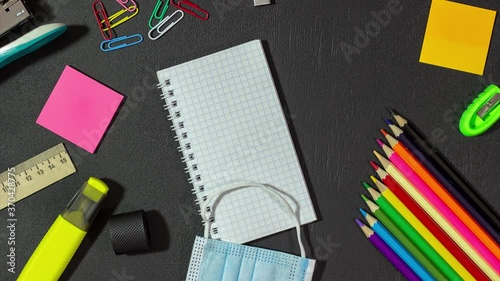 Stop motion animation: Medical mask and school supplies and a notebook on a black background. Mask from CHOVID-19 and stationery on a chalk board