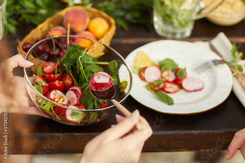 Close up of unrecognizable woman holding fresh vegetable salad while enjoying dinner with friends and family outdoors, copy space