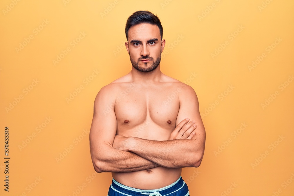 Young handsome man with beard wearing sleeveless t-shirt standing over yellow background skeptic and nervous, disapproving expression on face with crossed arms. Negative person.