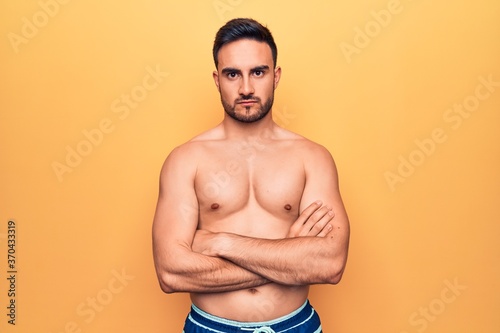 Young handsome man with beard wearing sleeveless t-shirt standing over yellow background skeptic and nervous, disapproving expression on face with crossed arms. Negative person.