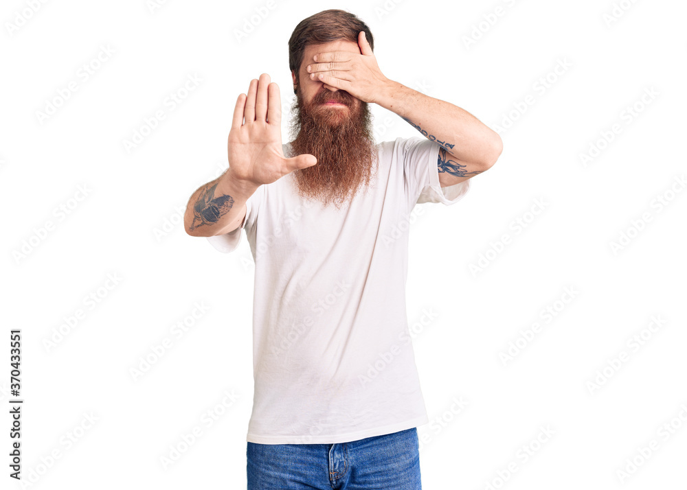Handsome young red head man with long beard wearing casual white tshirt covering eyes with hands and doing stop gesture with sad and fear expression. embarrassed and negative concept. Handsome young red head man with long beard wearing casual white tshirt covering eyes with hands and doing stop gesture with sad and fear expression. embarrassed and negative concept.