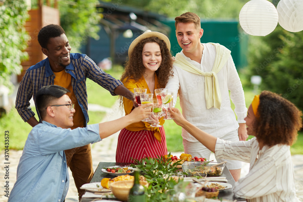 Obraz premium Multi-ethnic group of friends clinking glasses while enjoying dinner outdoors at Summer party, copy space
