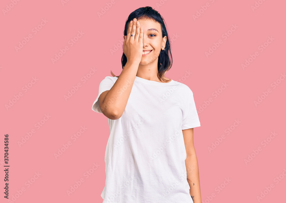 Young woman wearing casual clothes covering one eye with hand, confident smile on face and surprise emotion. Young woman wearing casual clothes covering one eye with hand, confident smile on face and surprise emotion.