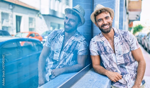 Young hispanic man on vacation smiling happy leaning on the wall at street of city