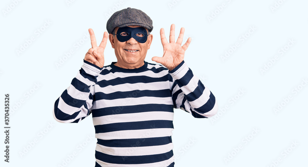 Senior handsome man wearing burglar mask and t-shirt showing and pointing up with fingers number seven while smiling confident and happy. Senior handsome man wearing burglar mask and t-shirt showing and pointing up with fingers number seven while smiling confident and happy.