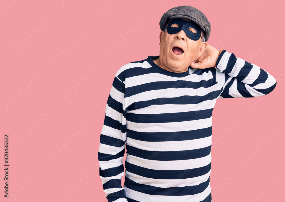Senior handsome man wearing burglar mask and t-shirt suffering of neck ache injury, touching neck with hand, muscular pain Senior handsome man wearing burglar mask and t-shirt suffering of neck ache injury, touching neck with hand, muscular pain