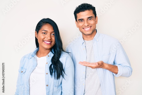 Beautiful latin young couple wearing casual clothes smiling cheerful presenting and pointing with palm of hand looking at the camera.