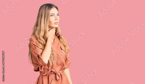 Beautiful caucasian woman with blonde hair wearing summer jumpsuit touching painful neck, sore throat for flu, clod and infection