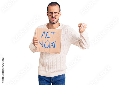 Young handsome man holding act now banner annoyed and frustrated shouting with anger, yelling crazy with anger and hand raised