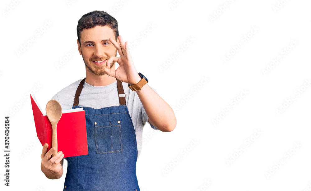 Handsome young man with bear wearing professional baker apron reading cooking recipe book doing ok sign with fingers, smiling friendly gesturing excellent symbol Handsome young man with bear wearing professional baker apron reading cooking recipe book doing ok sign with fingers, smiling friendly gesturing excellent symbol