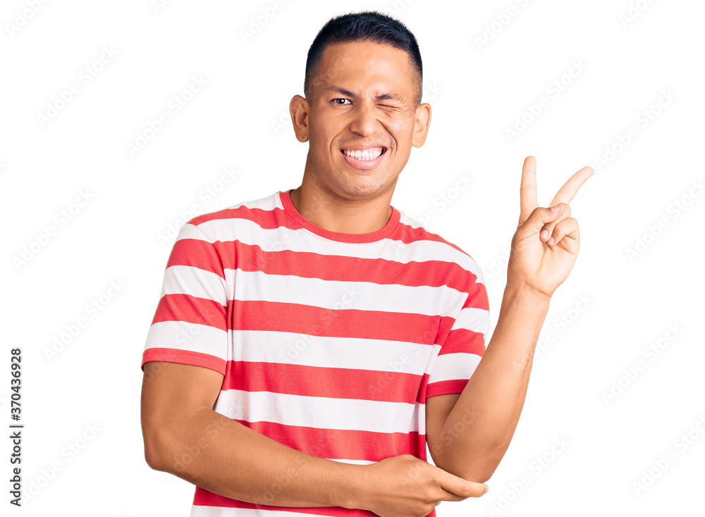 Young handsome latin man wearing casual clothes smiling with happy face winking at the camera doing victory sign. number two. Young handsome latin man wearing casual clothes smiling with happy face winking at the camera doing victory sign. number two.